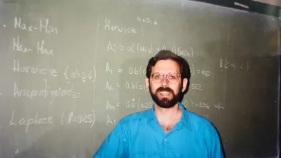 Photo of Bruce Stiftel as a young man standing in front of a green chalkboard