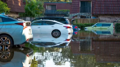 Parked cars in floodwater with two-story apartments or homes in background in Florida after hurricane.