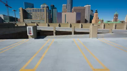 Empty parking spots on top floor of multistory garage with Minneapolis skyline in background.