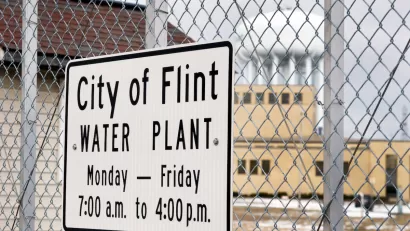 Close-up of sign on chain link fence "City of Flint Water Plant" with hours.