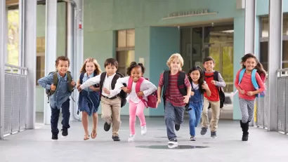 Group of elementary school children running in an outdoor corridor.