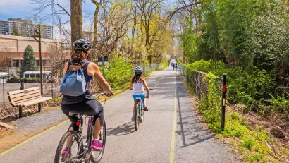 Family wearing helmets rides down separated bike trail in city.