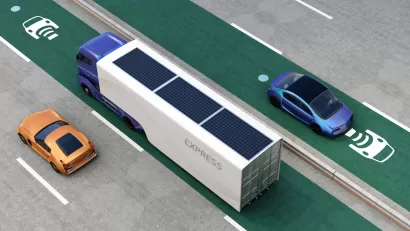 Rendering of truck and cars driving on green electric vehicle charging roadway lane.