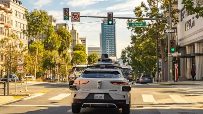 White Waymo self-driving taxi on street in downtown San Francisco, California with glass high-rise in background.
