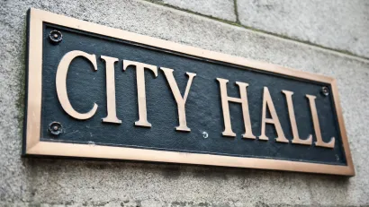 Close-up of "City Hall" plaque on building with gold lettering on black.