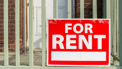 Close-up of red For Rent sign with white text on porck of brick building.