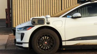 White Waymo self-driving car with camera and sensors mounted to front driver's side mirror.