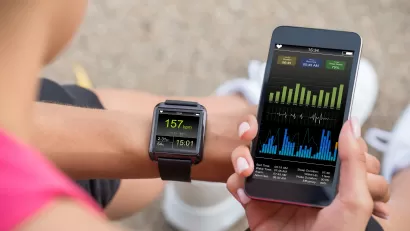 Close-up of person holding up phone and looking at their smart watch displaying fitness data