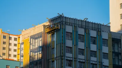 Construction workers on a suspended platform are installing thermal insulation on the facade of a modern apartment building, improving energy efficiency and reducing heat loss during cold weather.