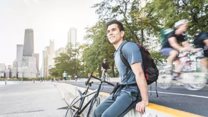 Man sitting on concrete wall with bike next to bike lane on Chicago waterfront.