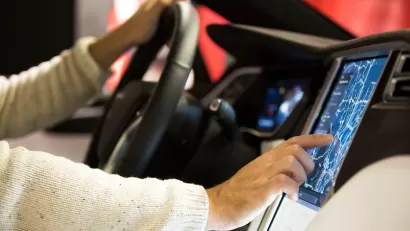 Close-up of man's hands on steering wheel and digital screen in Tesla car's driver's seat.