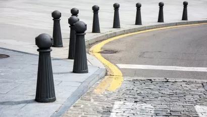Black bollards lining a curved sidewalk next to a cobblestone street.