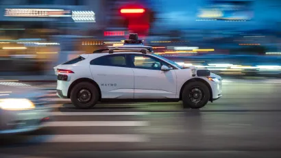 White Waymo autonomous car driving fast down city street with blurred background at night.