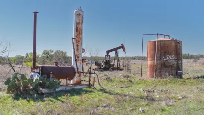Rusty abandoned oil well and equipment with prickly pear cactus next to it in West Texas.