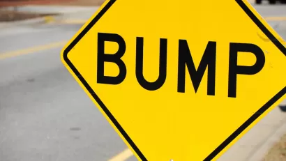 Close-up on yellow sign with black 'BUMP' letters indicating speed bump ahead.