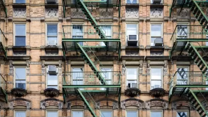 Brick New York City apartment building exterior with fire escape stairs and AC window units.