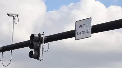 Traffic light on overhead pole with traffic camera and "Photo Enforced" sign