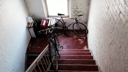 Two bicycles in apartment building stairwell landing with white painted brick walls.