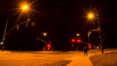 Intersection with stoplights at night with one pedestrian waiting to cross.