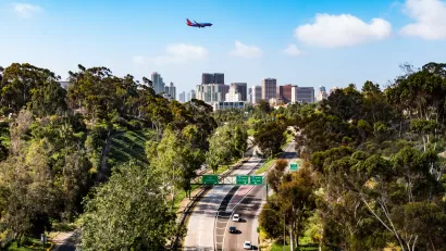 An airplane flies over the Cabrillo Freeway (State Route 163) as it passes through Balboa Park and into the downtown area of San Diego, California.