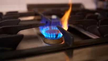 Close-up of lit burner on natural gas stove with blue flame and small yellow flame shooting up.