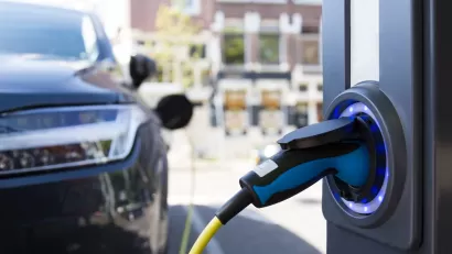 Close-up of electric car charging port with blurred dark colored car in background.