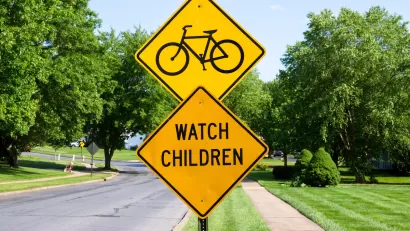 Yellow street sign with bike symbol above yellow 'Watch Children' sign.