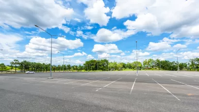 Empty large outdoor parking lot with green trees in background.