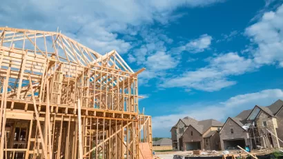 Wood-framed houses under construction with brick-covered completed homes in background.