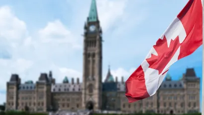 Canadian flag in foreground with blurred Canadian Parliament building in background in Ottawa, Ontario, Canada.