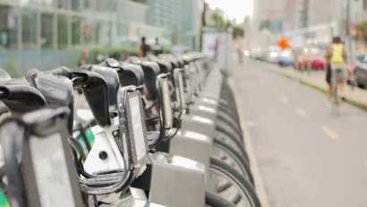 Close-up of silver Bixi bike share bikes parked at a station in Montreal, Quebec, Canada with blurred person on bike riding away in background.