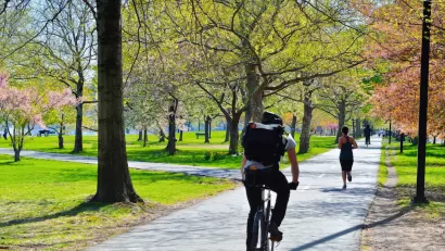 Cyclist and runner on paved bike and pedestrian path in a park in Boston with fall colors on trees.