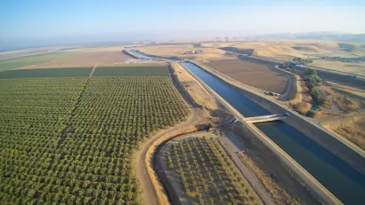 Aerial view of Claifornia aqueduct with green orchard on one side.