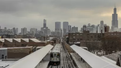Train on elevated track on snowy city landscape with Chicago skyline in background.