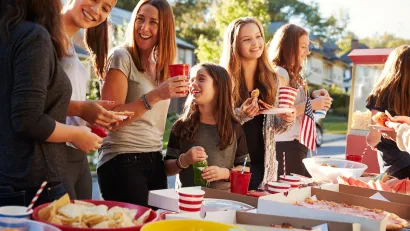 Group of people at table set ouf with picnic food on street during a neighborhood block party.