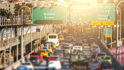 Rush hour traffic jam of cars, buses, taxis and trucks on the Williamsburg Bridge in Brooklyn, New York City with the colorful glow of sunlight in the background.