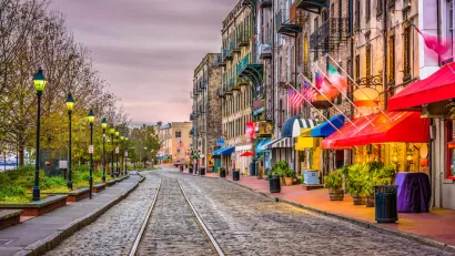 Cobblestone street with streetcar line, row of vintage streetlights on left, and colorful restaurant and shop awnings on right on River Street in Savannah, Georgia.