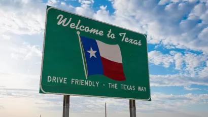 Green road sign with "Welcome to Texas" above Texas flag and "Drive Friendly - the Texas Way" below.