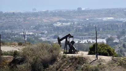Oil well on hilltop in Los Angeles with city neighborhoods in background.