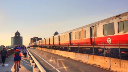 Cyclists and a red T train on the Longfellow Bridge in Boston, MA at sunset.
