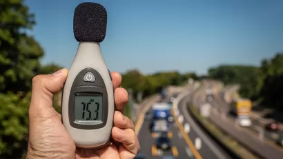 Close-up of hand holding up decibel meter with blurred highway with traffic in background