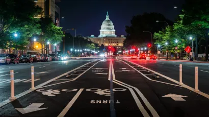 Low view of separated bike lanes in middle of Pennsylvania Avenue with U.S. Capitol dome visible at end of street at night.