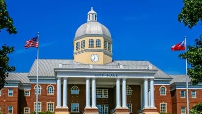 Neoclassical city hall building with dome, columns, and American flags flying in front