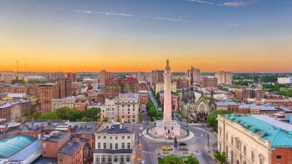 Aerial view of downtown Baltimore, Maryland with prominent statue in foreground at dusk.