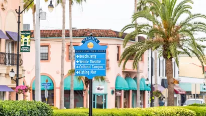 Street sign in Venice, Florida planned community with pink Italianate buildings and palm trees in background.