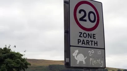 Close-up of white 20 kph speed limit sign in Europe with cartoon turtle and '20 is plenty' sticker underneath.