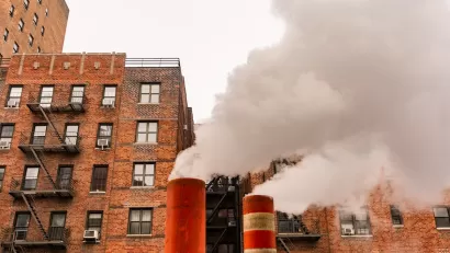 Orange and white steam pipes in New York City releasing white steam against background of red brick buildings.