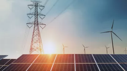 Solar panels, wind turbines, and power line tower against sunset sky.