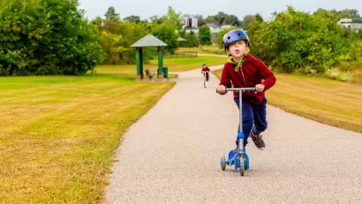 Young child riding scooter on gravel path in park.