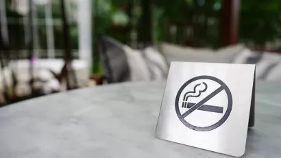 Close-up of silver sign indicating 'no smoking' with cigarette inside circle with line. Sign is sitting on patio table outdoors.